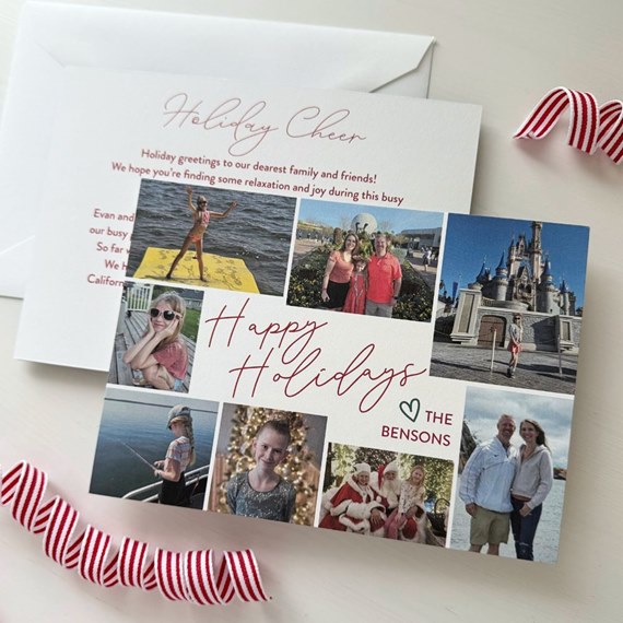 Square holiday collage photo card with multiple family photos, red handwritten 'Happy Holidays' text, personalized family name line, and white envelope on a table.