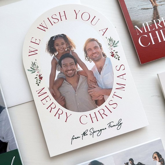 arched personalized Christmas photo card with oval family photo, red circular greeting text and holly accents
