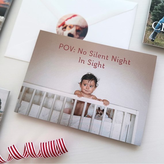 Holiday photo card featuring a baby standing in a white crib with the caption 
