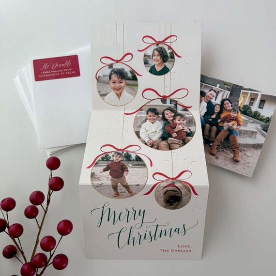Folded Christmas photo card with circular ornament photo frames, red bows, green 'Merry Christmas' script and inserted family photos