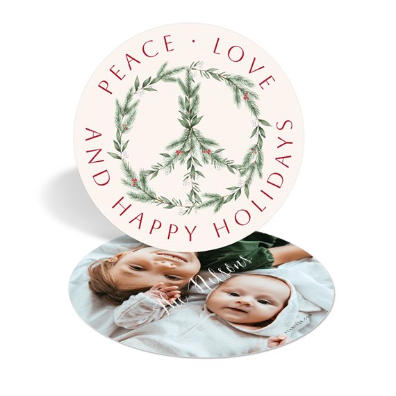 Round holiday card with pine-wreath peace sign and red 'Peace · Love · And Happy Holidays' text; reverse side shows a photo of two infants.