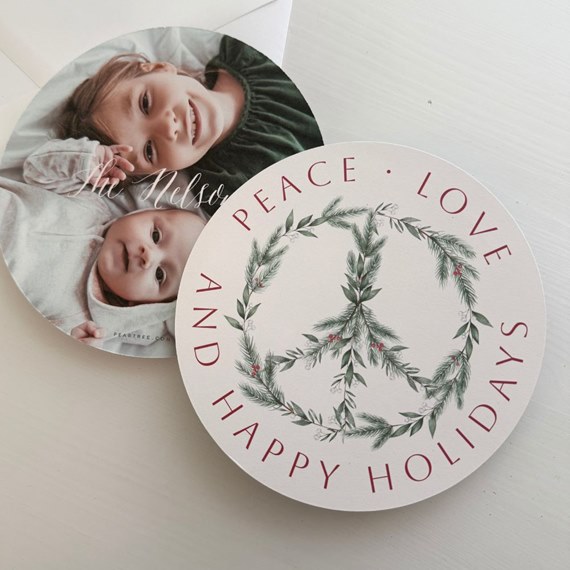 round holiday card with greenery peace-sign wreath and red holiday text, paired with a round photo card of two children