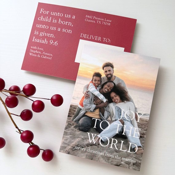 Christmas postcard with family portrait on front over a beach sunset and white "Joy to the World" text; red back side displays a scripture verse and address area.