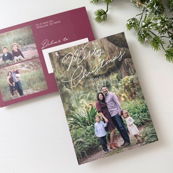 Christmas photo postcard with family portrait, white script greeting and burgundy envelope