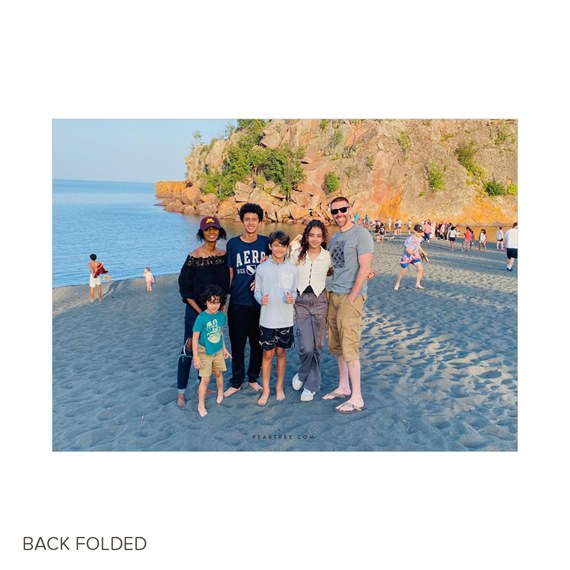 Family of six posed on a sandy beach with ocean and rocky cliff behind them