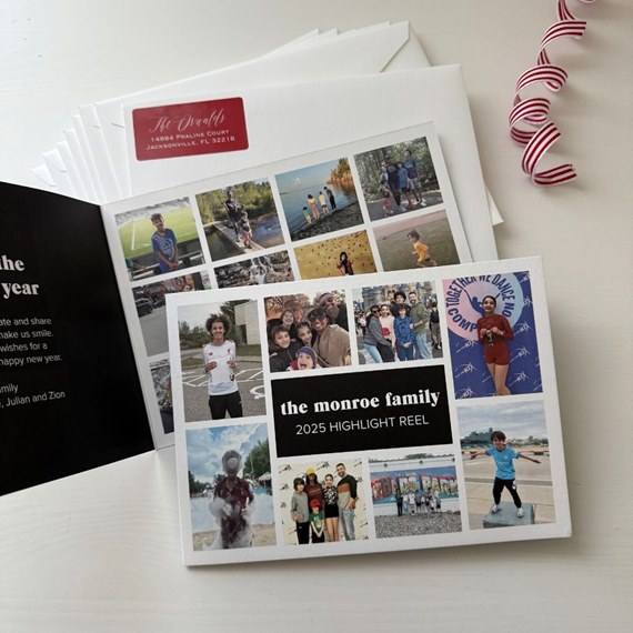 square photo-collage greeting card with black center title band and multiple family photos, shown with white envelopes and a red-striped ribbon