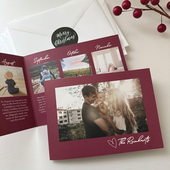 A4 folded burgundy Christmas photo card with family photos, white handwritten-style text and signature, shown with white envelopes and a Merry Christmas sticker.
