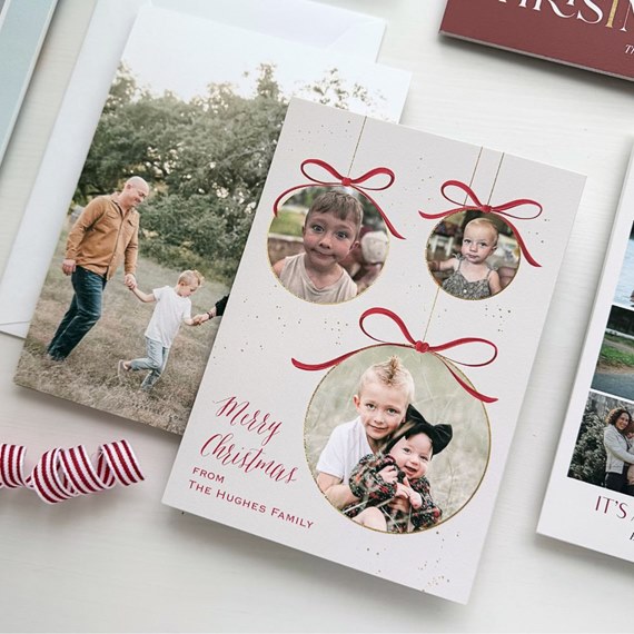 Folded Christmas photo card with three ornament-shaped photo frames, red bows, gold accents and a holiday greeting on a white background