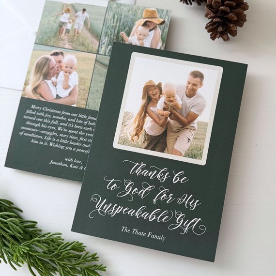 dark green folded Christmas photo card with white script text and centered family photograph; back shows photo collage and holiday message