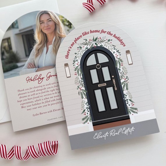 Arch-shaped holiday business card with illustrated black door, evergreen garland, red berries, neutral siding background and circular photo headshot insert.