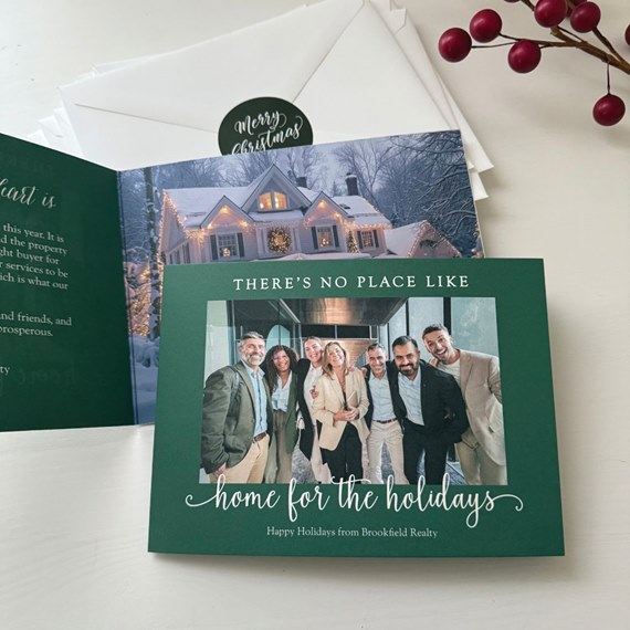 dark green folded holiday business card with group photo and snowy house interior, accompanied by white envelopes