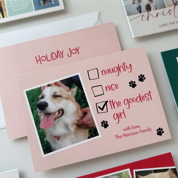 pink holiday card with dog photo, checklist showing 'the goodest girl' checked, red text and paw print accents